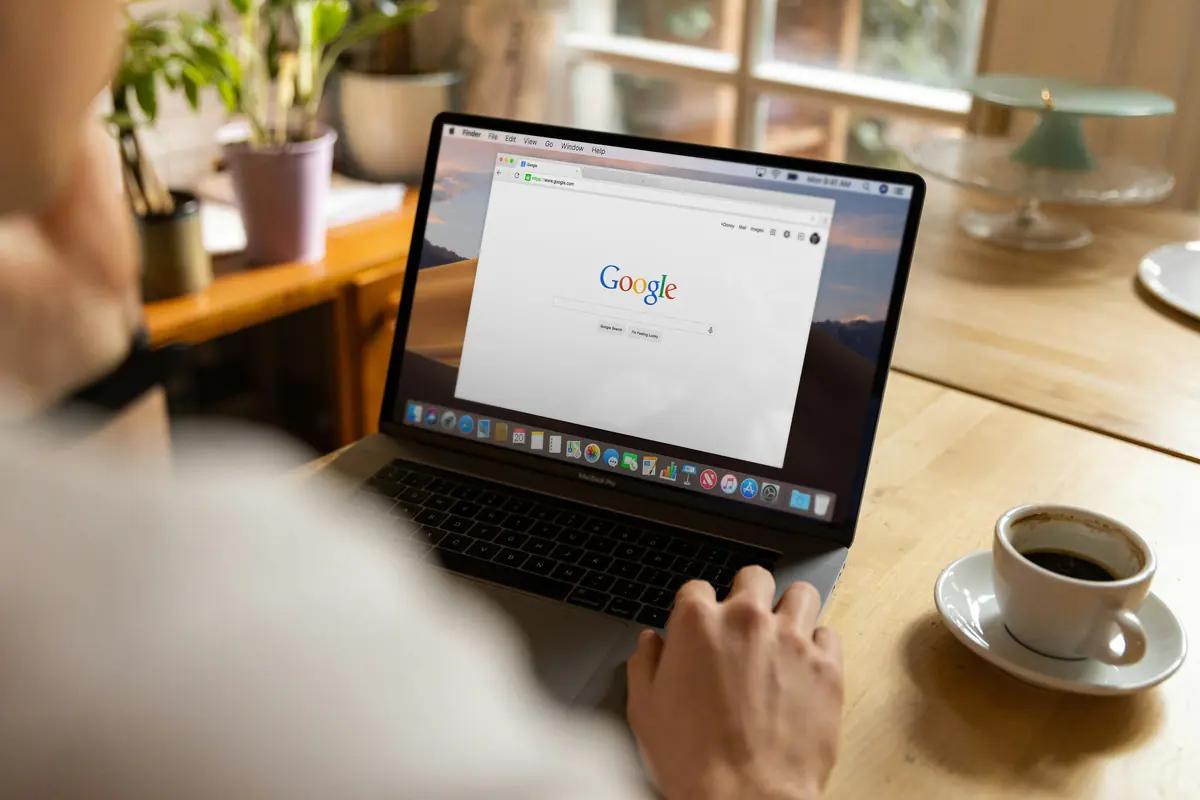 Pessoa usando um notebook com a página inicial do Google aberta, ao lado de uma xícara de café.