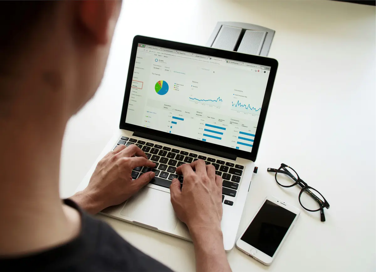 Pessoa digitando em um notebook com um painel de métricas e gráficos na tela.